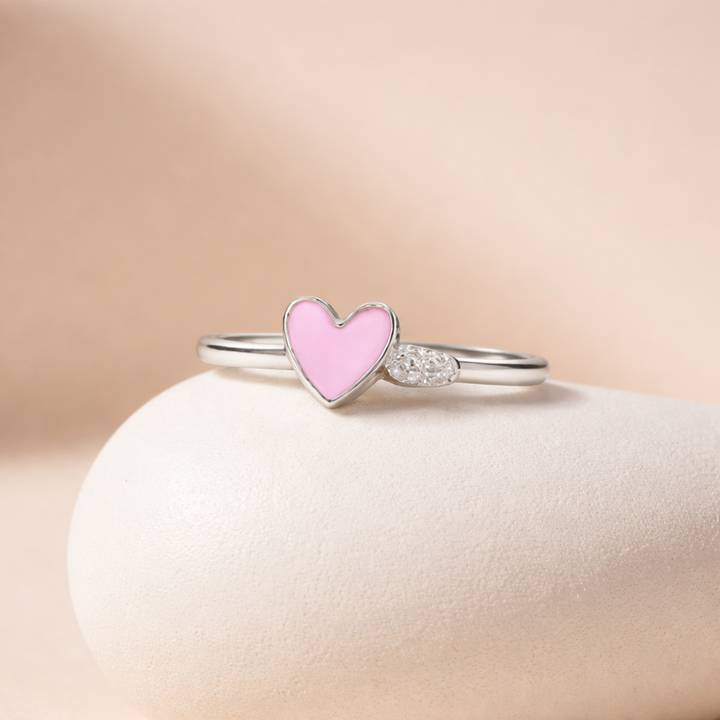 Silver ring with a pink heart-shaped gemstone on a beige background