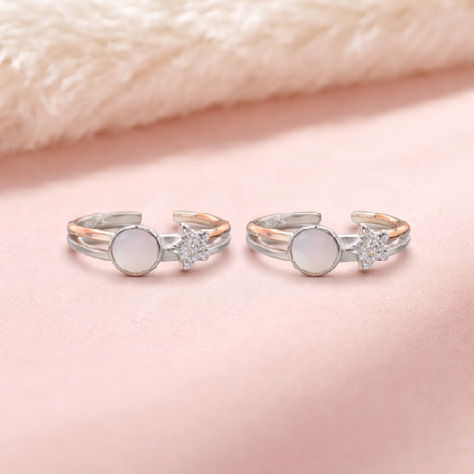 Two silver toe rings with gemstones on a soft pink background
