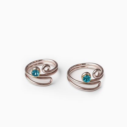 Two silver wire-wrapped toe rings with blue gemstones on a white background