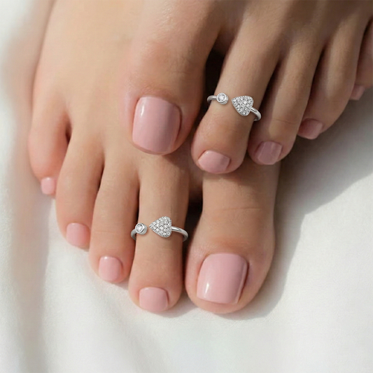 Silver toe rings on toes with pink nail polish on a white background