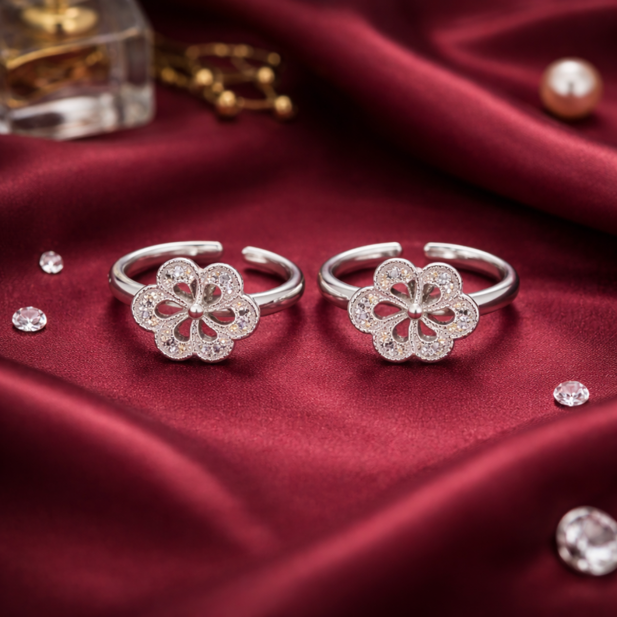 Two silver flower-shaped rings on a red fabric background with small crystals.