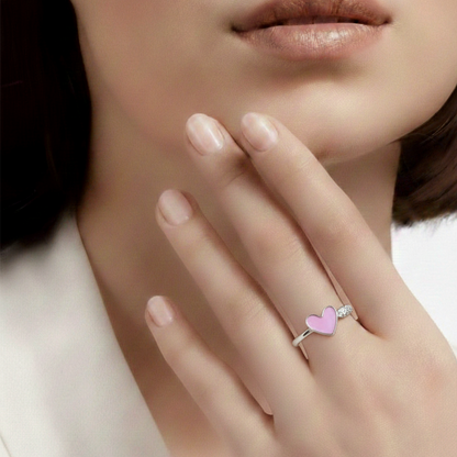 Close-up of a hand wearing a ring with a pink heart on a neutral background