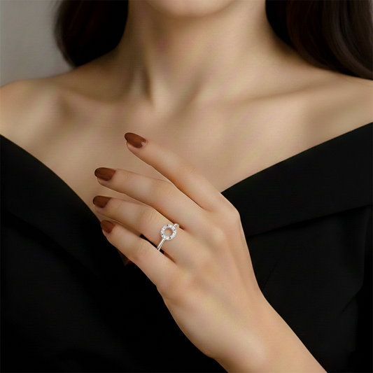 Close-up of a hand wearing a silver ring with a flower design, against a neutral background.