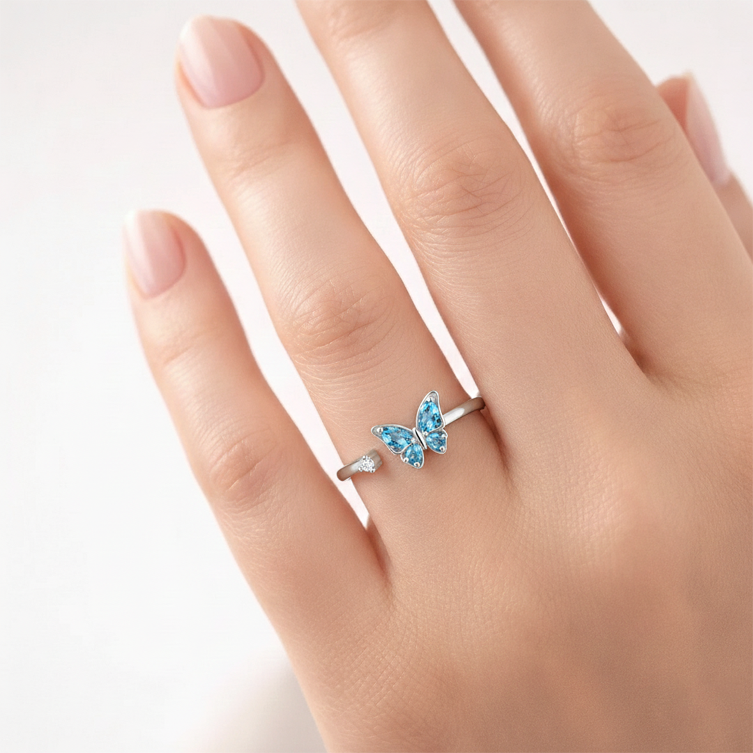 Butterfly-shaped ring with blue gemstones on a hand against a white background
