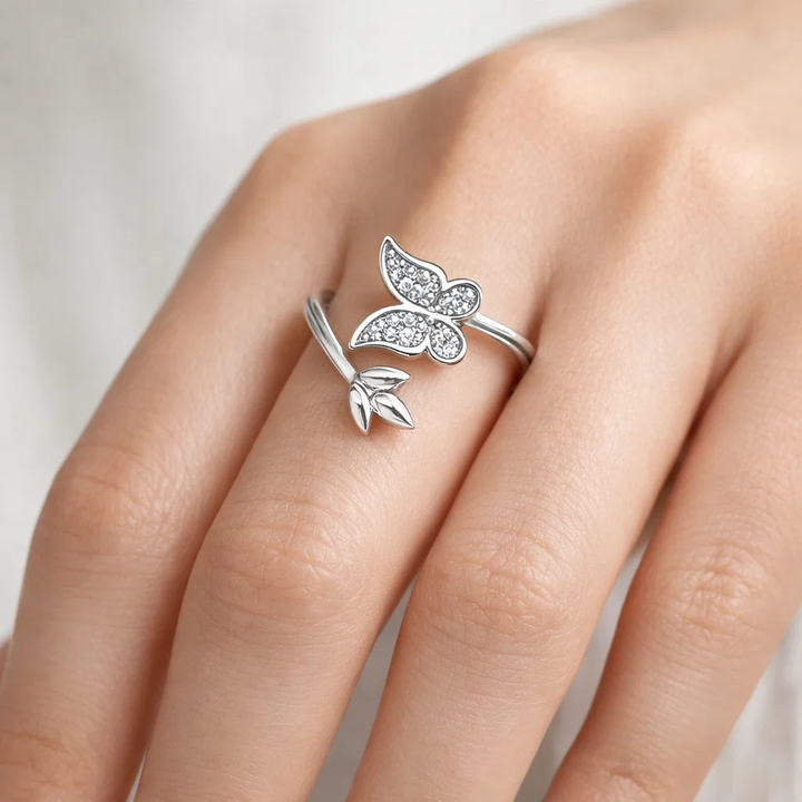 Silver butterfly ring on a person's finger against a neutral background