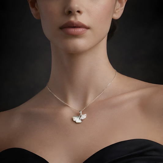 Woman wearing a delicate necklace with a leaf pendant against a dark background