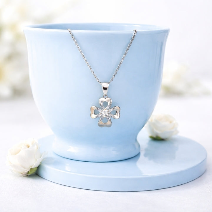 Silver necklace with a clover pendant on a light blue stand with white flowers in the background