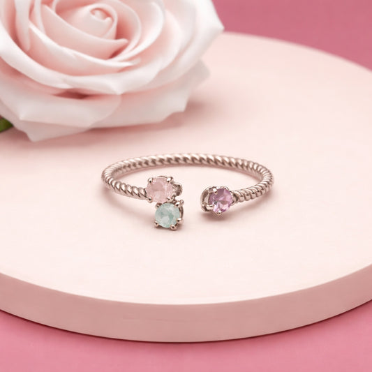 Silver ring with pink and green gemstones on a pink surface with a white rose.