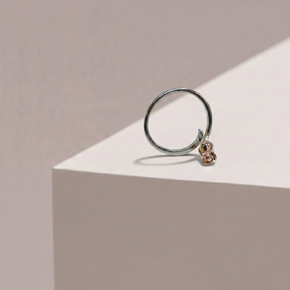 Silver ring with a small rose gold heart charm on a beige background