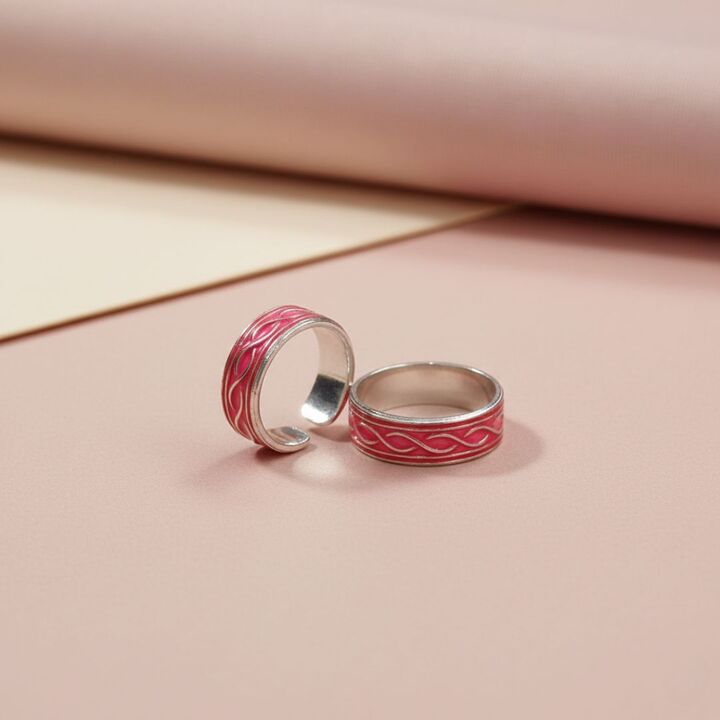 Two silver rings with red enameled designs on a pink background
