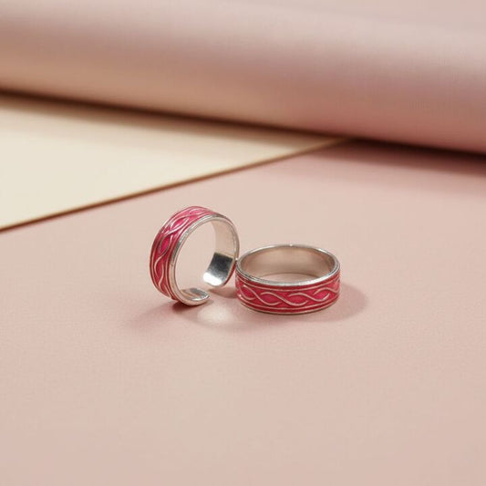 Two silver rings with red enameled designs on a pink background