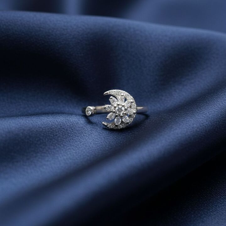 Silver moon-shaped ring with embedded stones on a blue fabric background