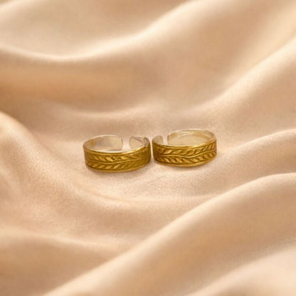 Two gold rings with intricate designs on a beige fabric background