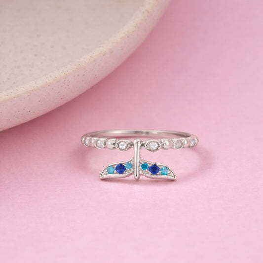 Silver ring with a whale tail design on a pink background