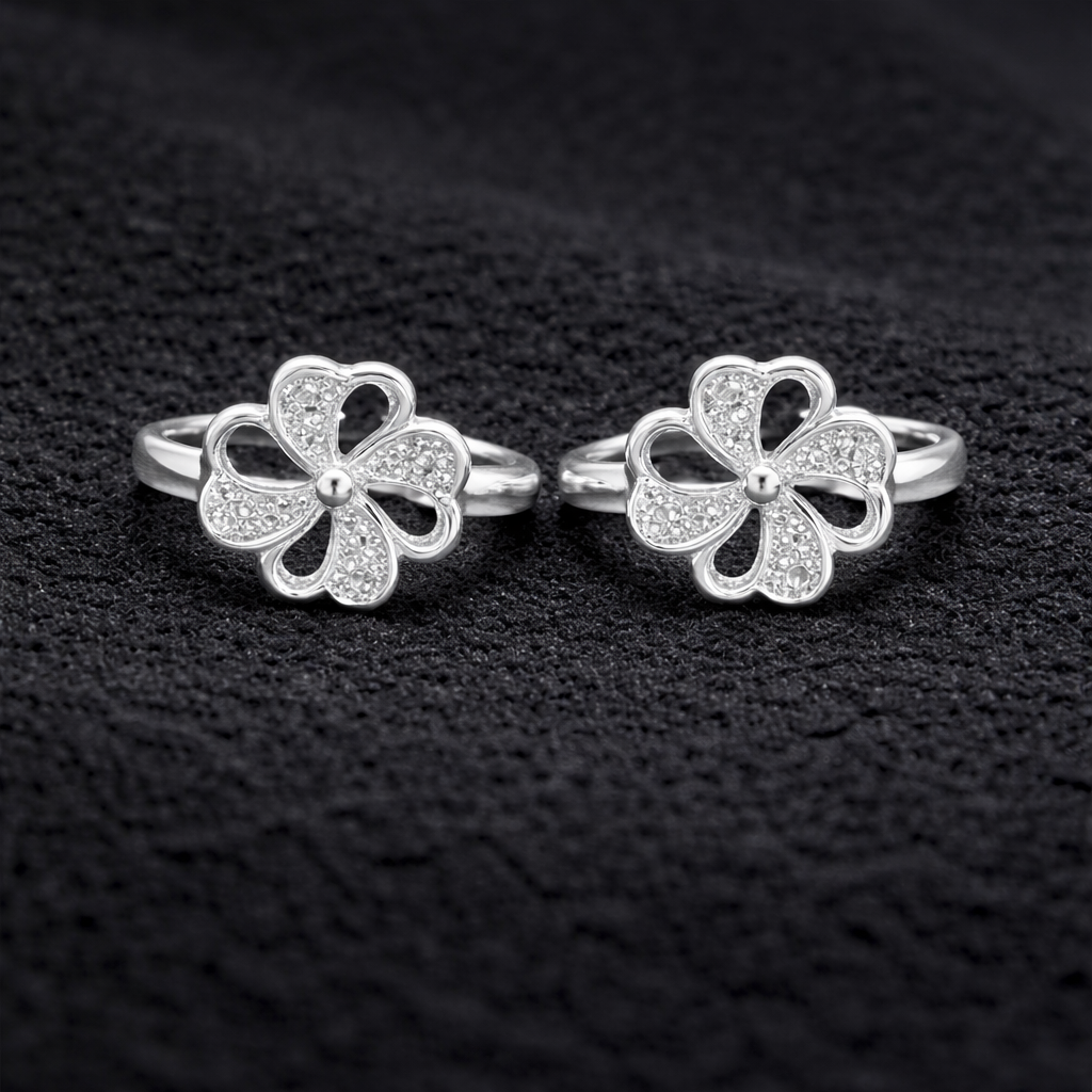 Two silver four-leaf clover toe rings on a black textured background